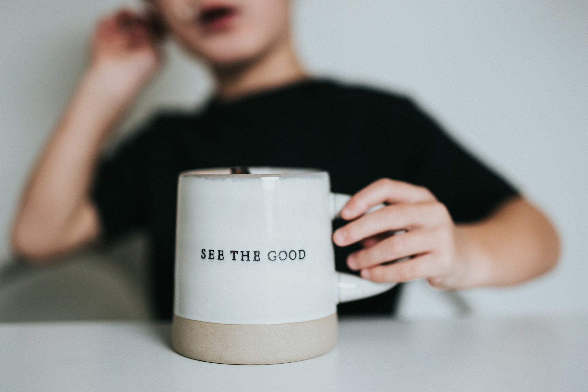 Child holding 'See the Good' mug.