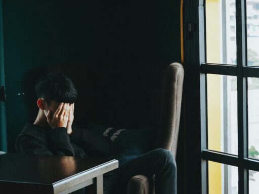 Person sitting, face in hands, near window.